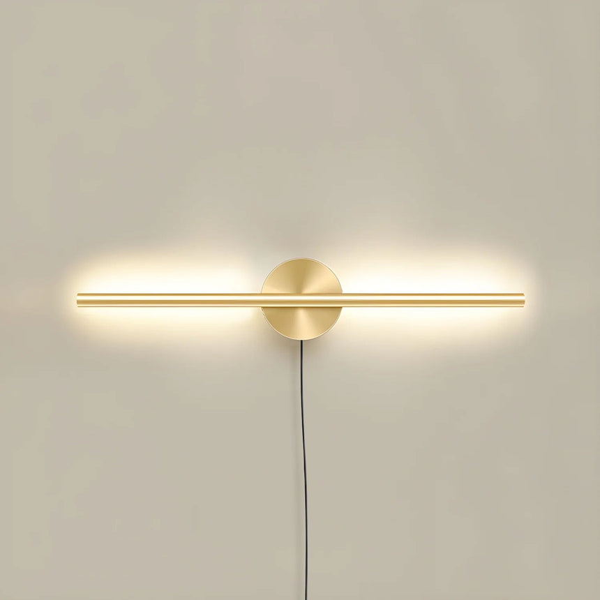 The taller gold profile lit on a pale wall, the cord dropping below the plate