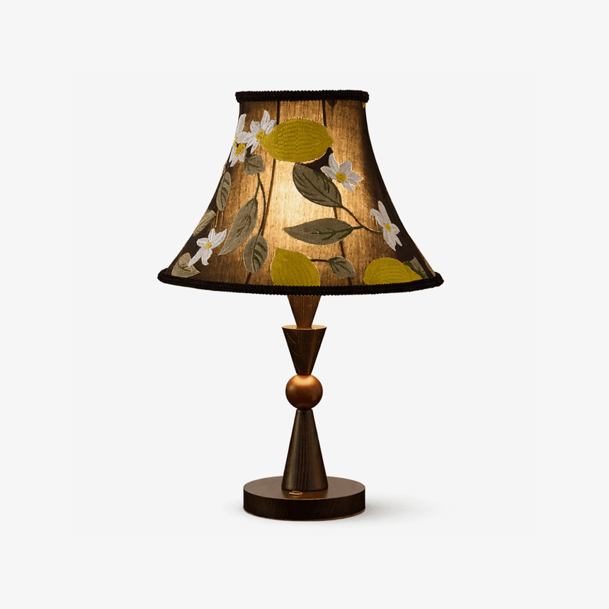Black table lamp with an embroidered shade on a turned wood stem, plain background