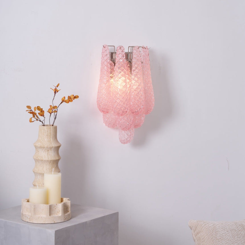 The pink sconce lit above a side table with candles and a vase