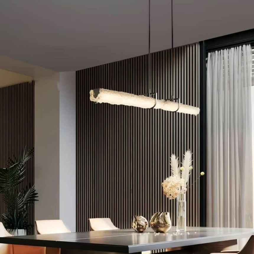 The glass branch lit above a dining table against a dark ribbed wall