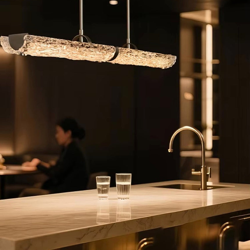 The glass branch lit above a kitchen island beside the tap