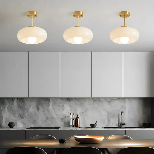 Three white glass domes on brass stems lit above a dark kitchen counter