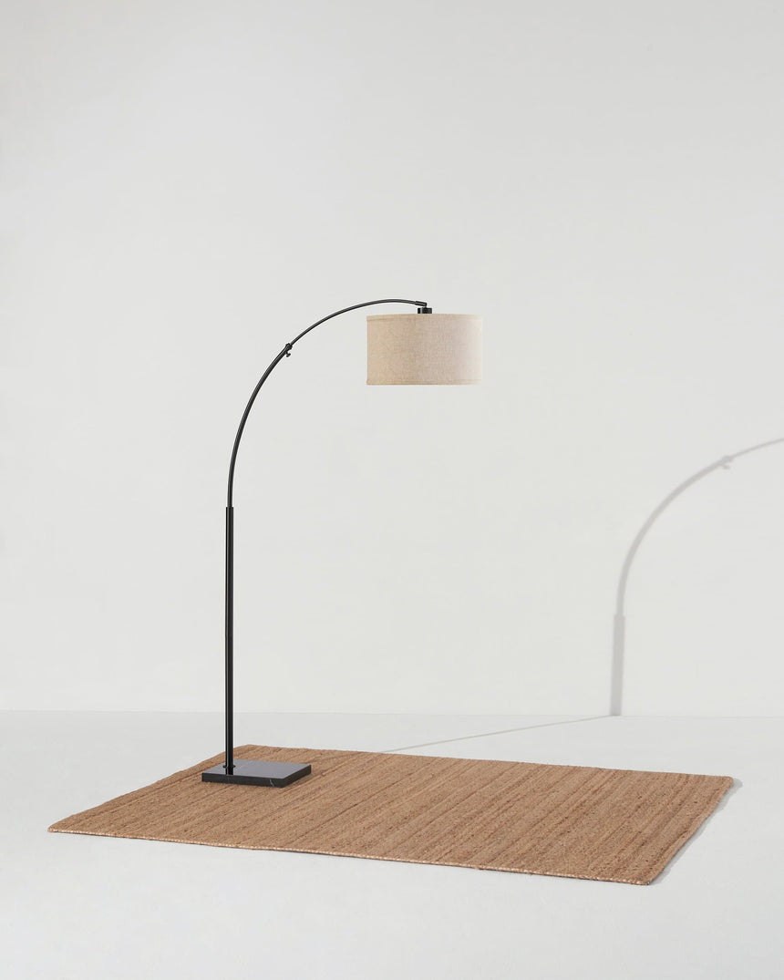 Black arc lamp on a woven rug, the base set behind the line of the shade