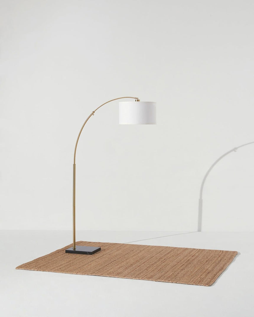 Brass arc lamp standing on a woven rug, the shade tipped over the floor