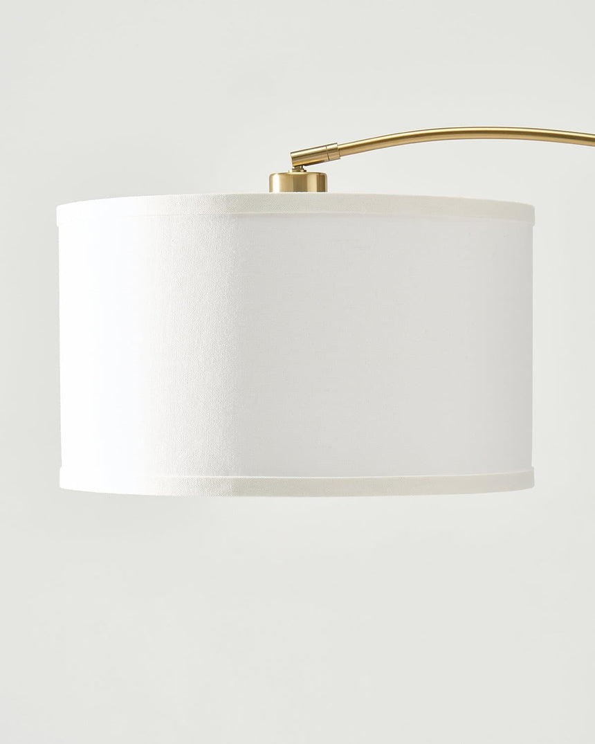 The brass arm entering the top of the white drum shade at a fixed collar