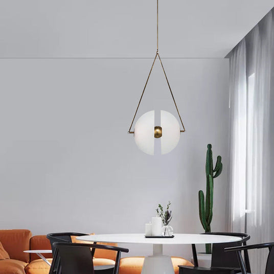 The framed glass disc lit above a dining table with a cactus by the window