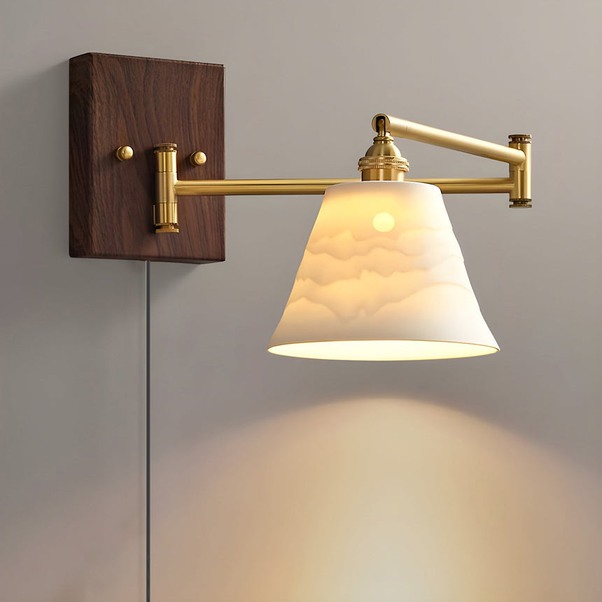 Ceramic bell shade lit on a brass arm over a walnut plate, cord below