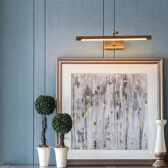 Bronze bar lit over a framed canvas on a blue panel wall between two topiary trees