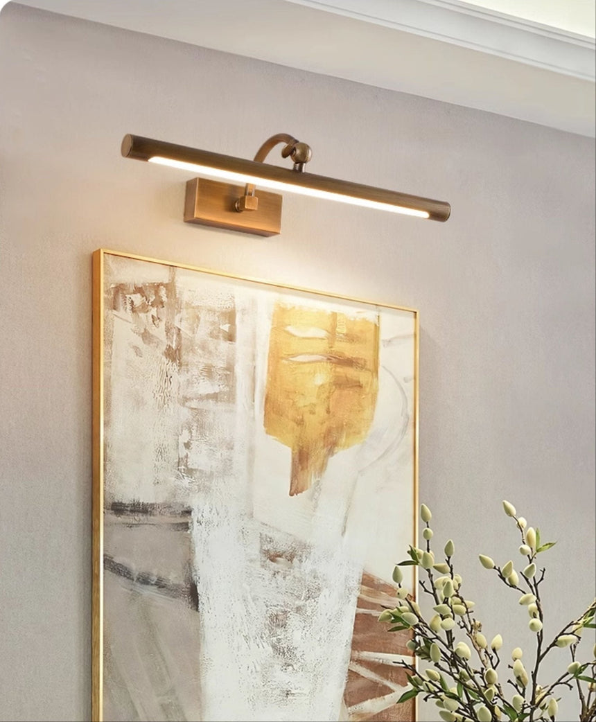 Bronze bar lit over a gilt framed canvas beside a branch of small leaves