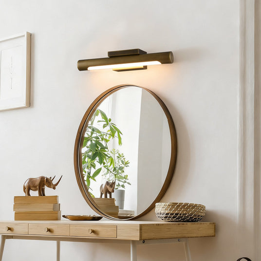 Bronze bar above a round mirror over a console with books and a plant