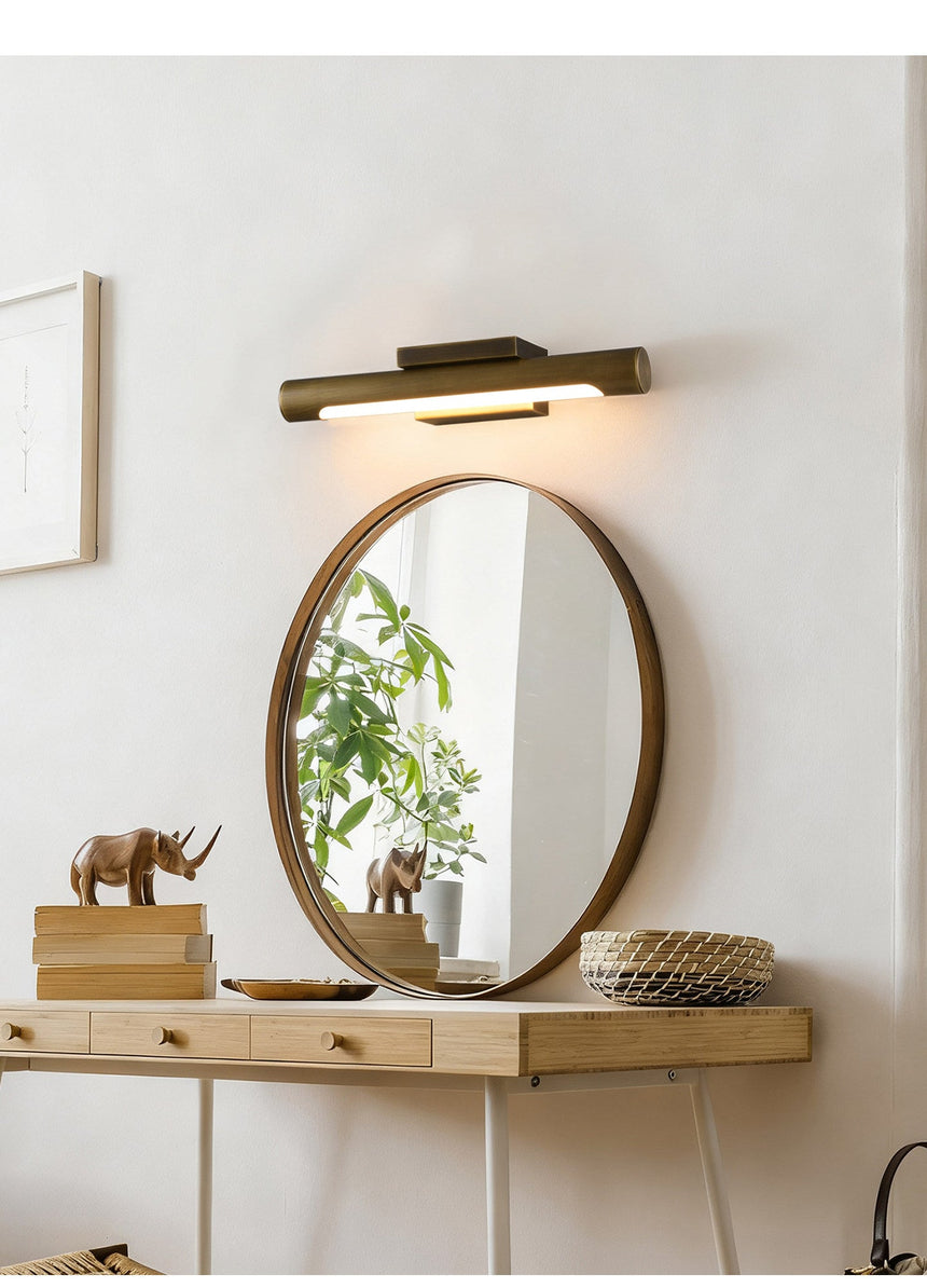 Bronze bar lit above a round mirror on a pale wall beside a framed print