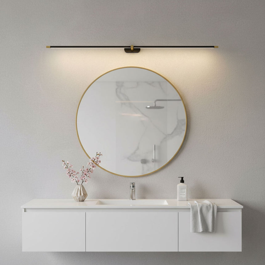 Slim rod lit above a round brass mirror over a white vanity unit with a towel