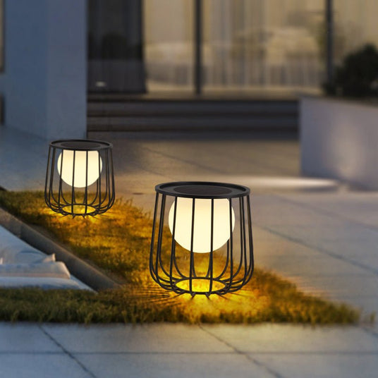 Two cage lanterns lit on grass beside the paved entrance to a house