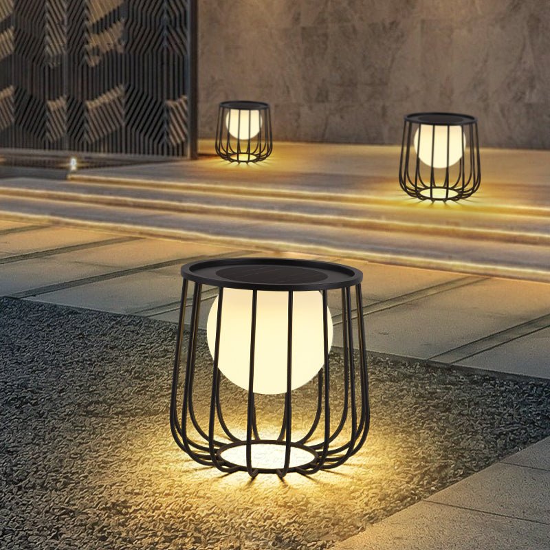 Two cage lanterns lit on gravel beside pale steps in a dark garden