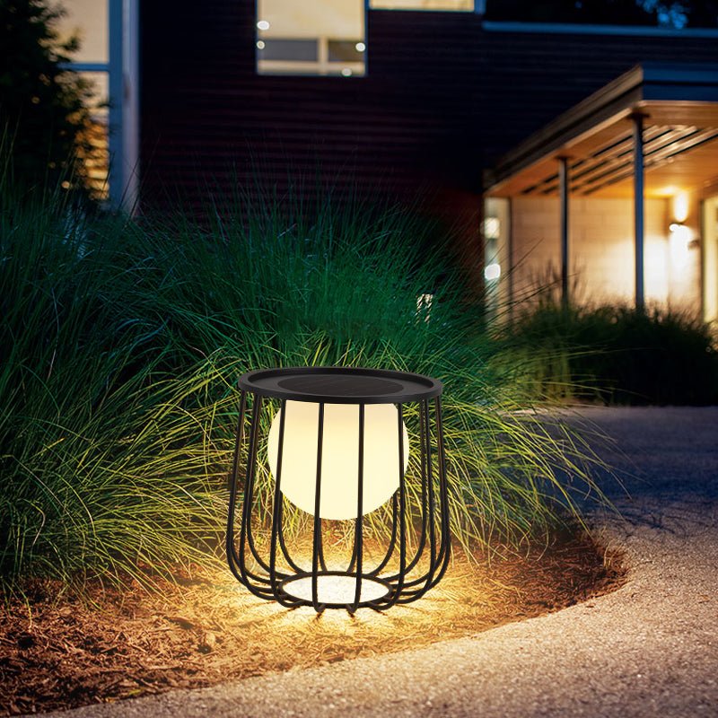 The cage lantern lit among ornamental grasses at the edge of a path