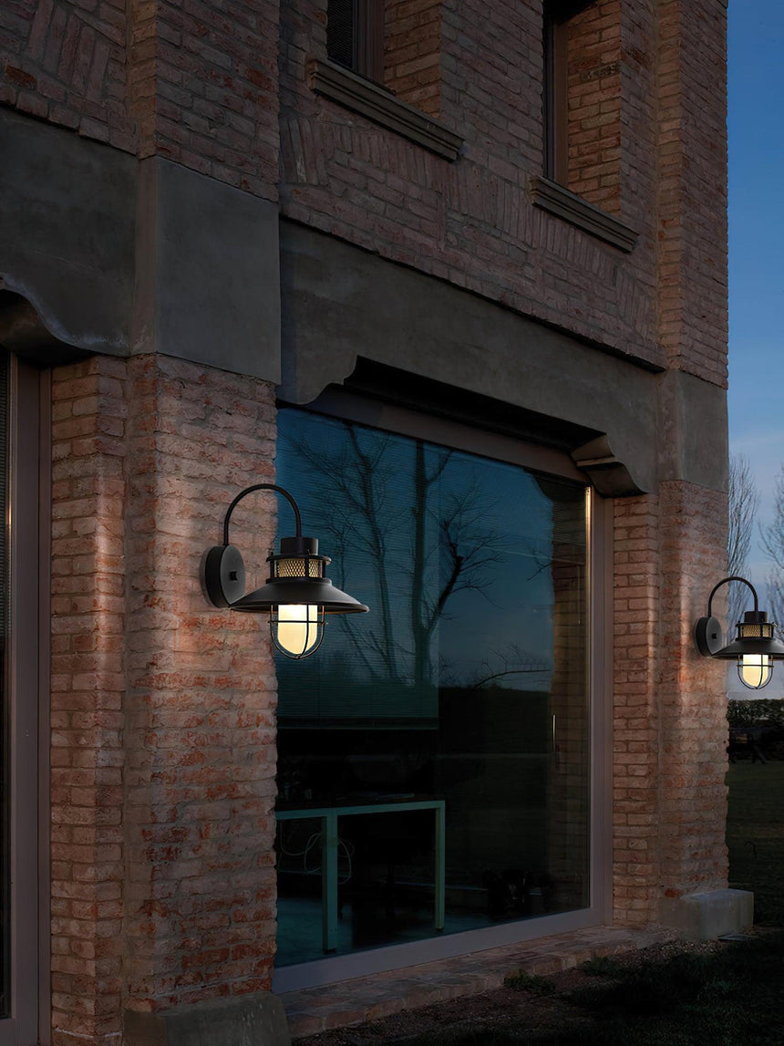 Sconces lit on a brick facade either side of a large window at dusk
