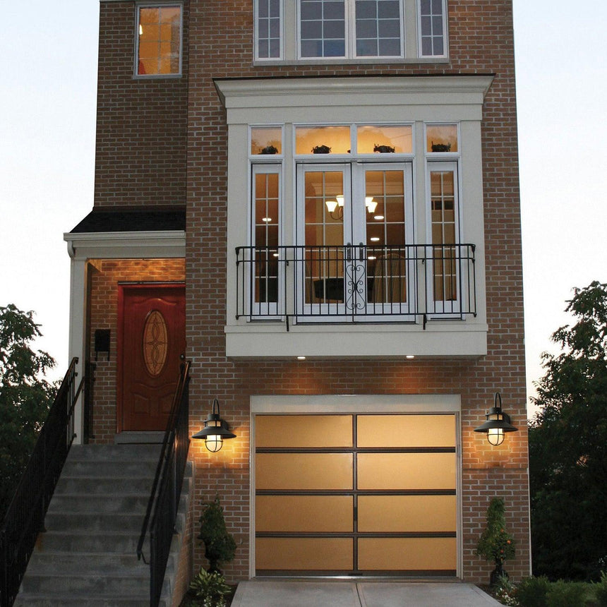 Cage sconces lit on either side of a garage door below a brick townhouse, steps to the entry