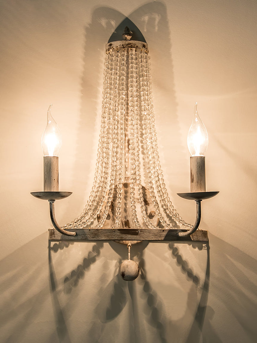 The sconce lit warm, the arms and strands casting soft shadows on the wall