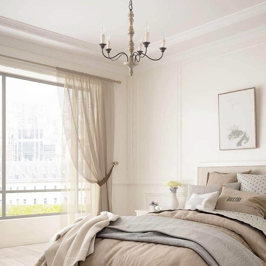 Lit in a bedroom above the foot of a made bed, long curtains and a framed picture nearby