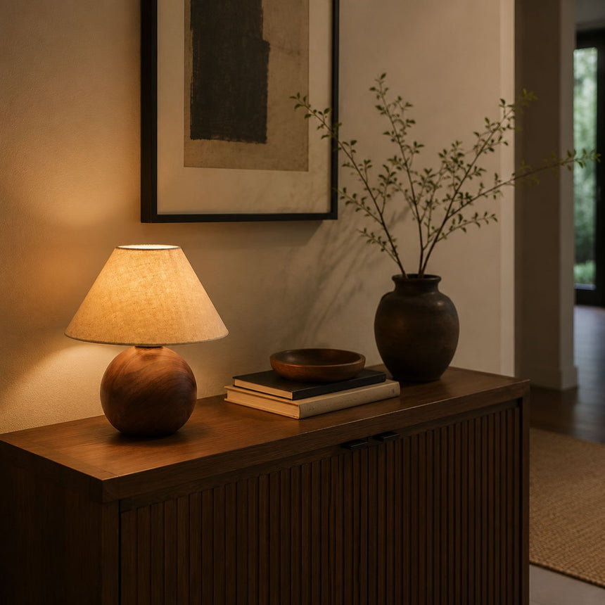 Ceramic bedside lamp lit on a sideboard beside a dark vase and books