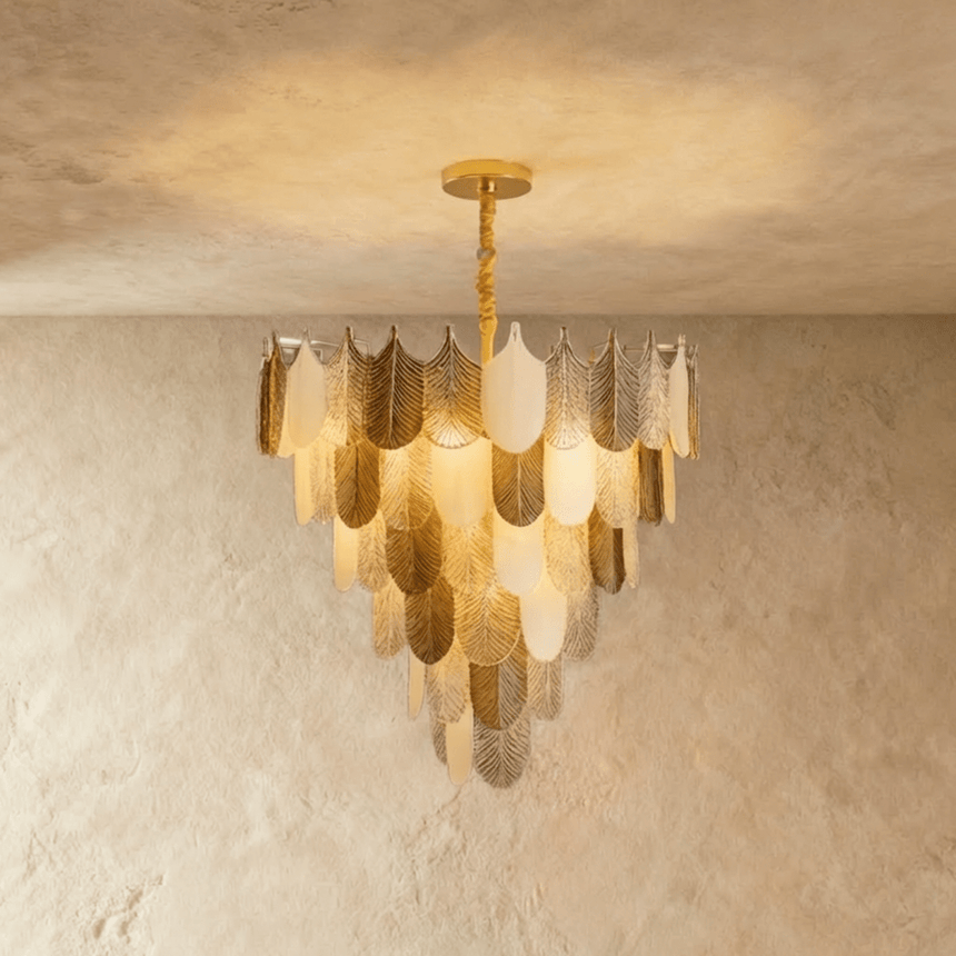 A round chandelier of tiered gold and white feather shaped glass shades, lit