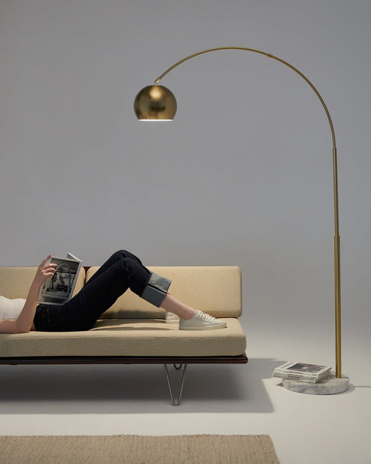 Brass arc lamp reaching over a low daybed, a reader lying under the dome