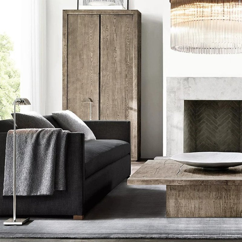 The lit lamp beside a dark sofa with a throw, a fireplace and a low table beyond