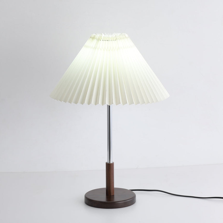 Chrome stem table lamp lit with a cooler light, pleats reading as lines