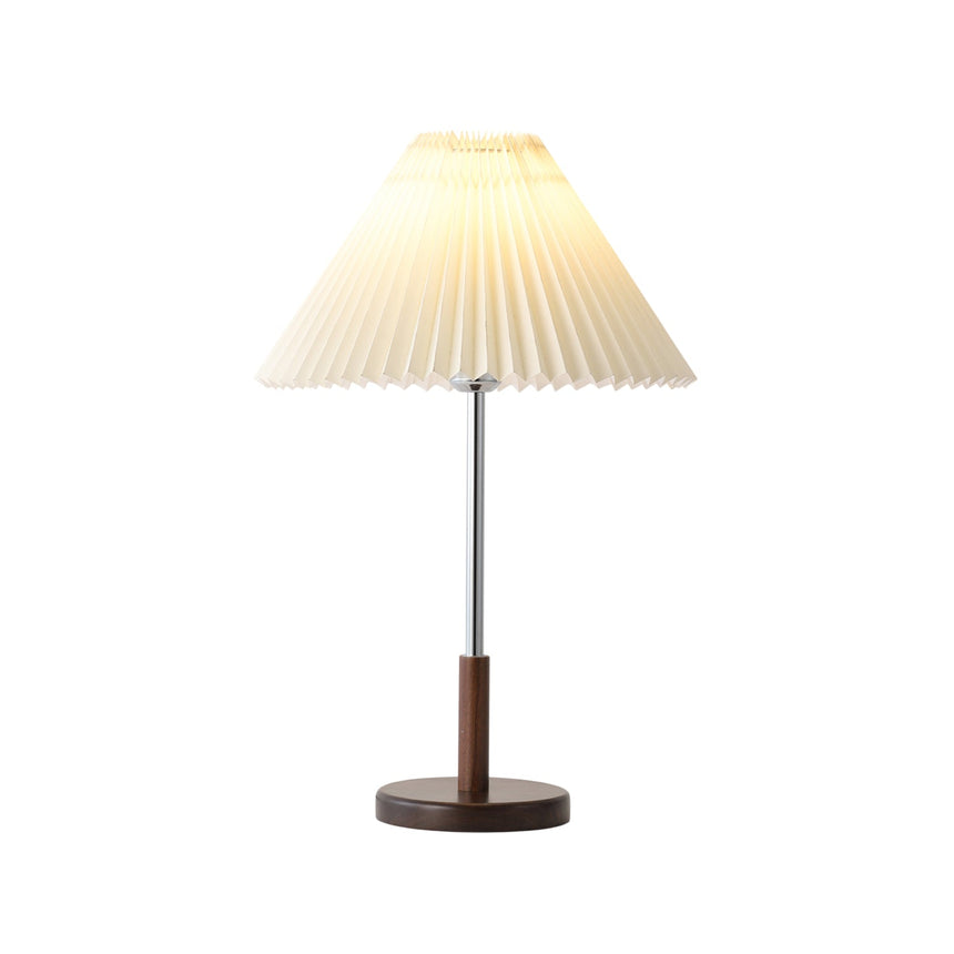Chrome stem table lamp lit front on, the pleated shade glowing softly