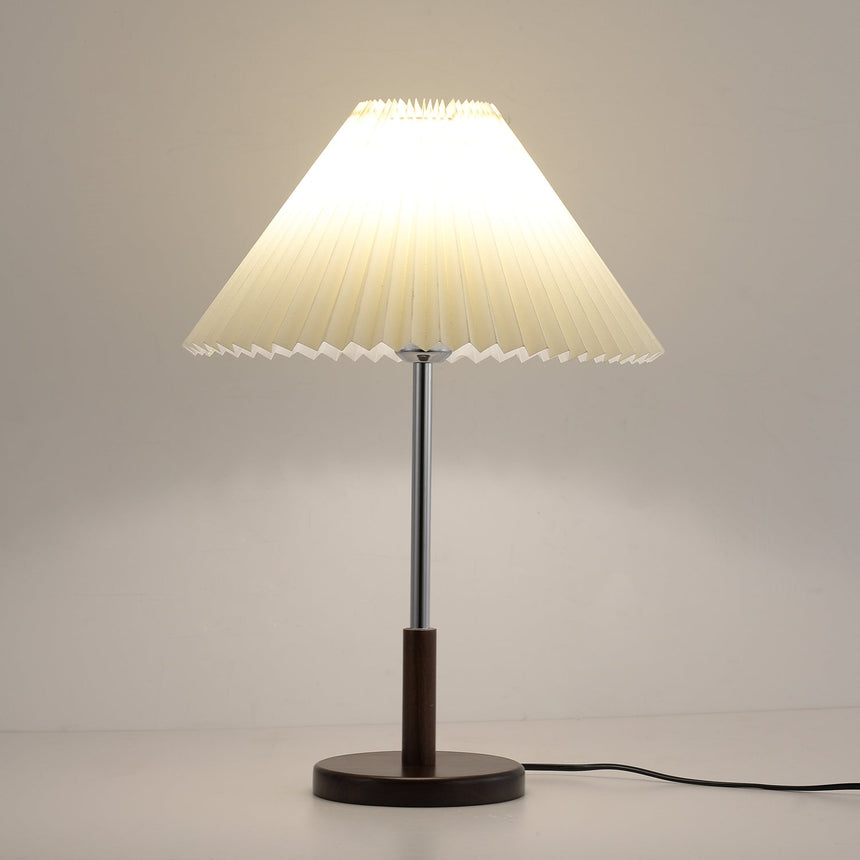 Chrome stem table lamp lit against a warm ground, the shade glowing amber