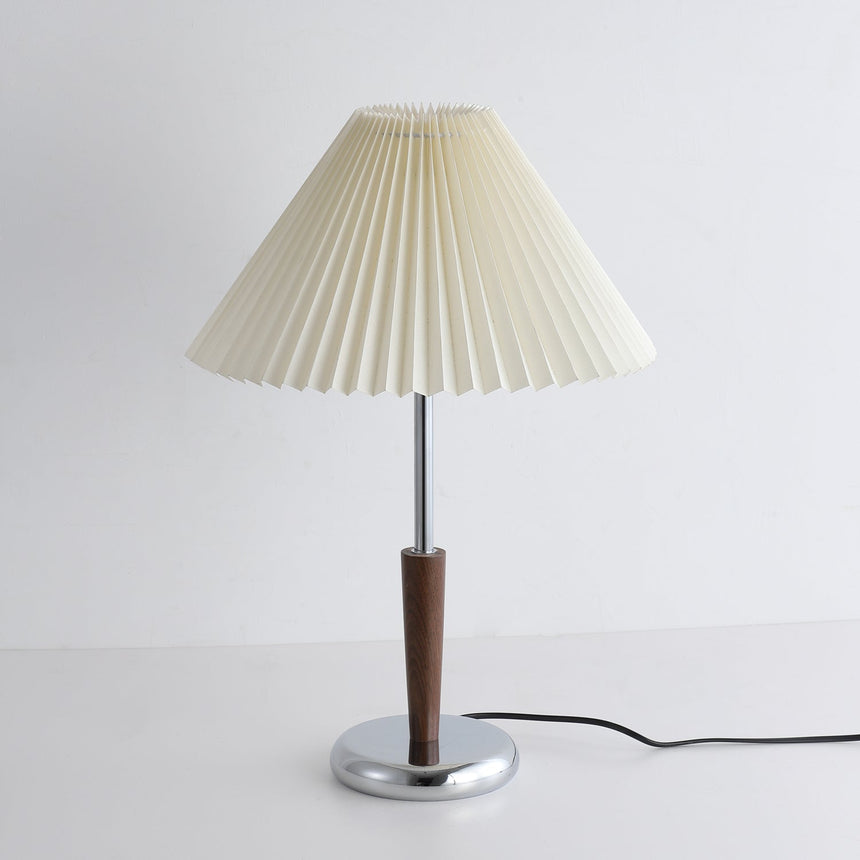 Chrome table lamp seen from the front, pleated shade above the chrome foot