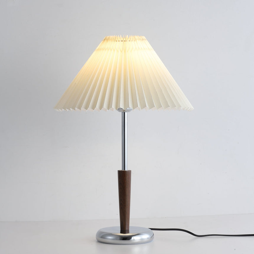 Chrome table lamp unlit in a pale room, walnut stem visible