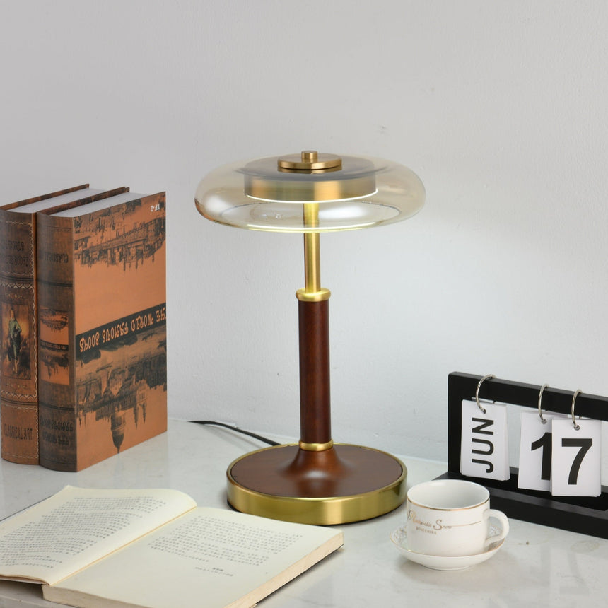 Glass disc lamp lit with a cooler light beside bound books