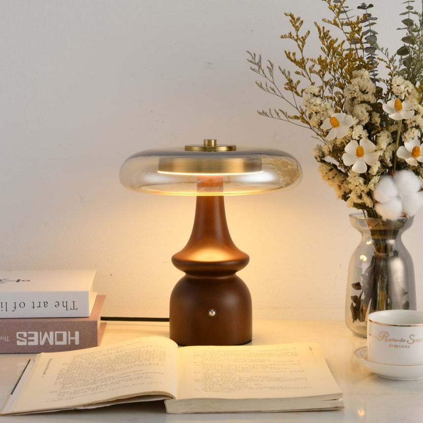 Clear glass table lamp lit over an open book beside flowers