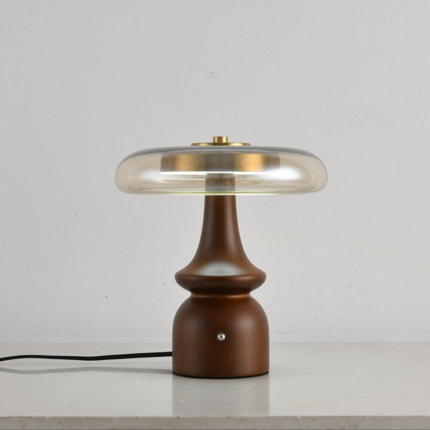 Clear glass table lamp on a spindle base, lit on a plain ground