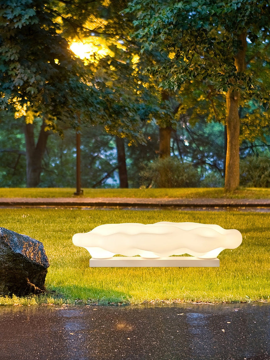 The cloud lit on grass beside a dark boulder and a paved edge