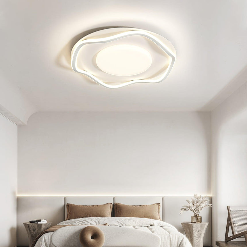 Cloud shaped ceiling lamp above a bed with a bolster cushion and a dried branch
