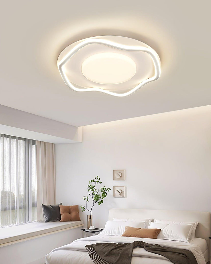 Cloud shaped ceiling lamp lit above a bed with a plant and framed pictures on the wall