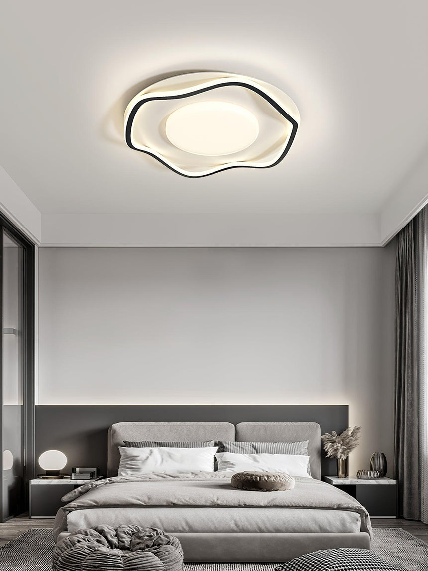 Cloud outline ceiling lamp above a bed with a gray upholstered headboard and curtains