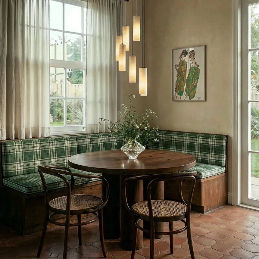 Lit cylinders above a round dining table with chairs and a banquette by a window