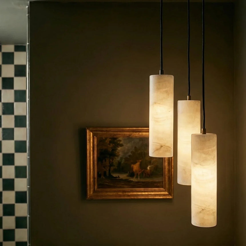 Three lit cylinders hung beside a framed painting on a deep green wall