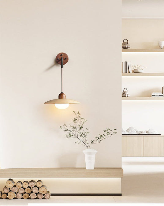 Sconce lit above a bench of logs and a vase of branches before open shelves