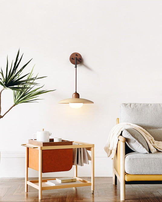 Sconce lit above a wood trolley with a plant beside a sofa and a throw