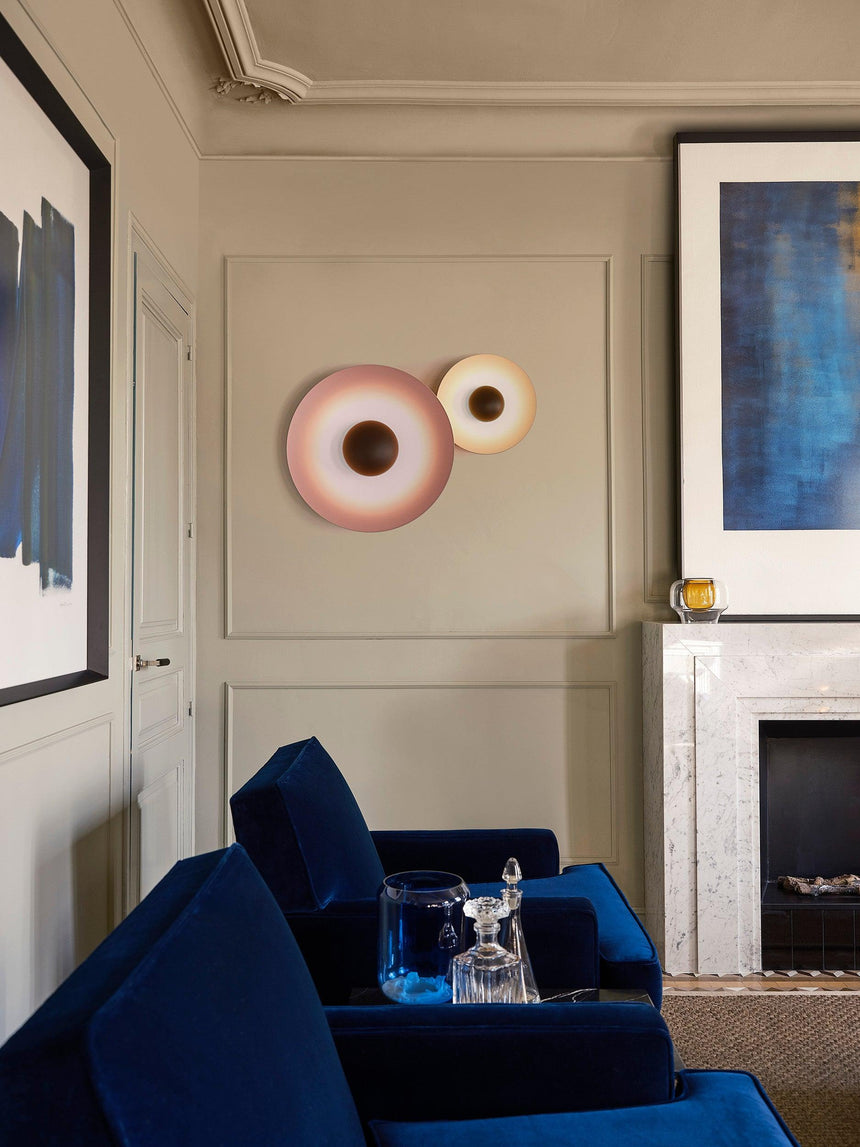 A pair of discs lit above a navy armchair beside a fireplace