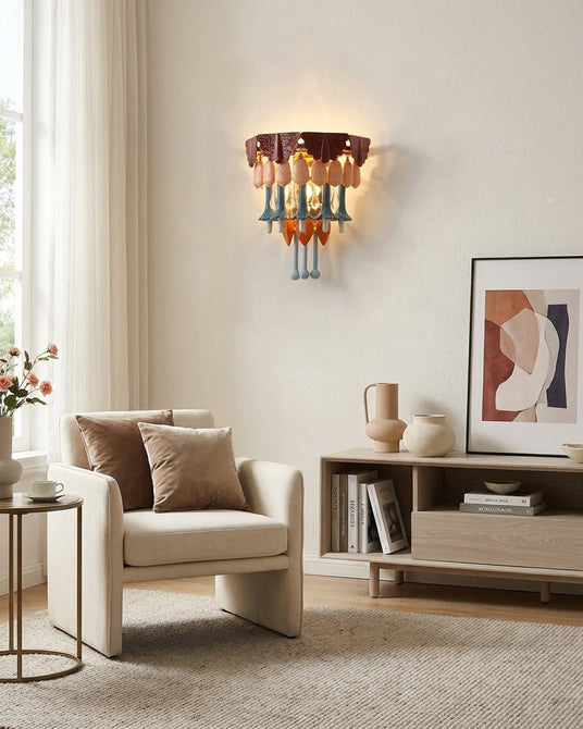 The ceramic fringe sconce lit above a cream armchair and a low shelf of books