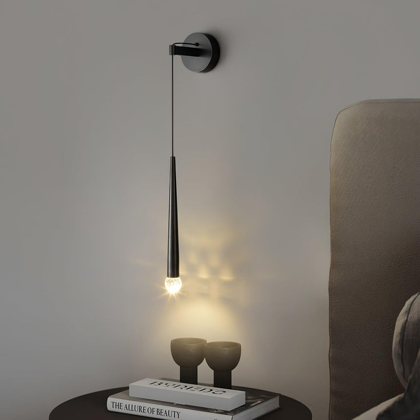 The black cone lit above a round nightstand with two vases beside a headboard