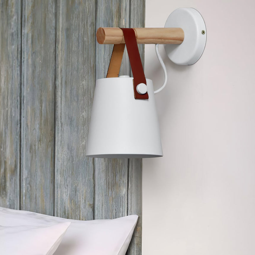 White cone lit on a weathered plank wall above a bed with white linen