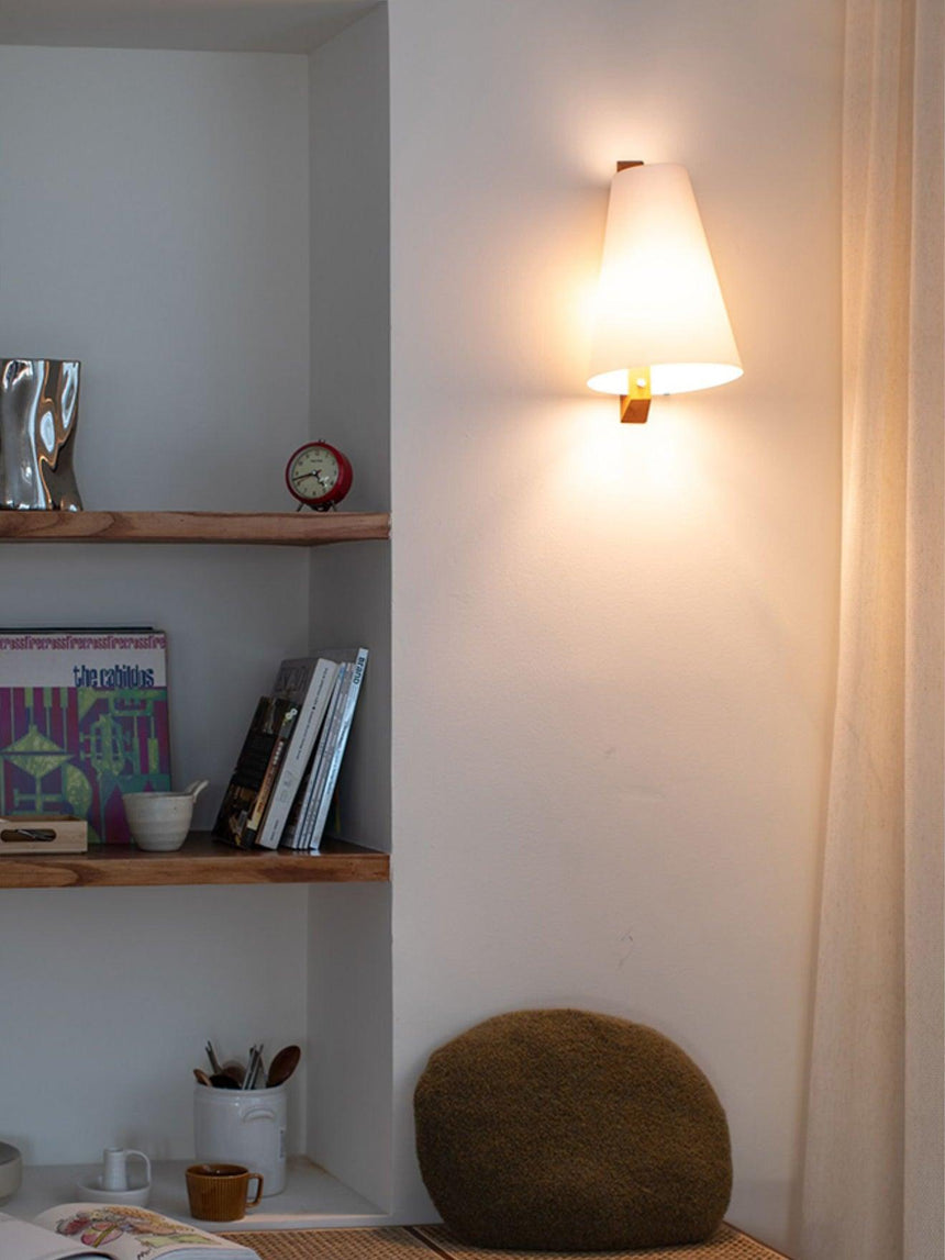 Sconce lit beside built in shelves holding books and a stone bowl