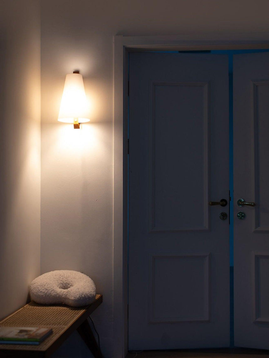 Sconce lit beside a panel door above a low bench with a round cushion
