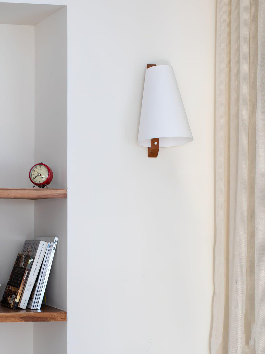 Sconce lit above a narrow shelf holding books and a small round clock
